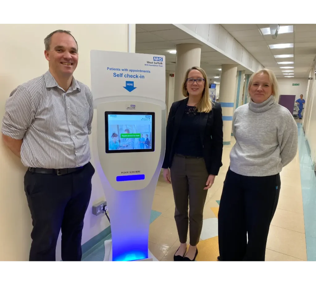 3 Adults standing next to a Computer screen kiosk at West Suffolk Hospital