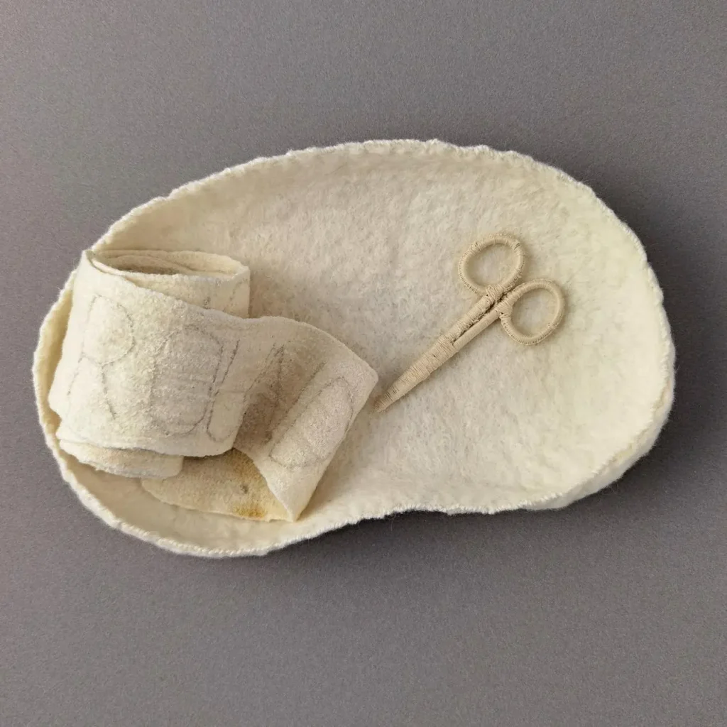 Felted and embroidered artwork of a nurses kidney dish, bandage and scissors