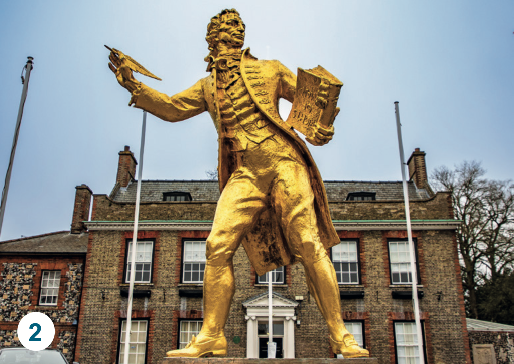 The Thomas Paine statue outside King's House in Thetford, painted gold and holding a quill and papers, standing in front of the historic building.