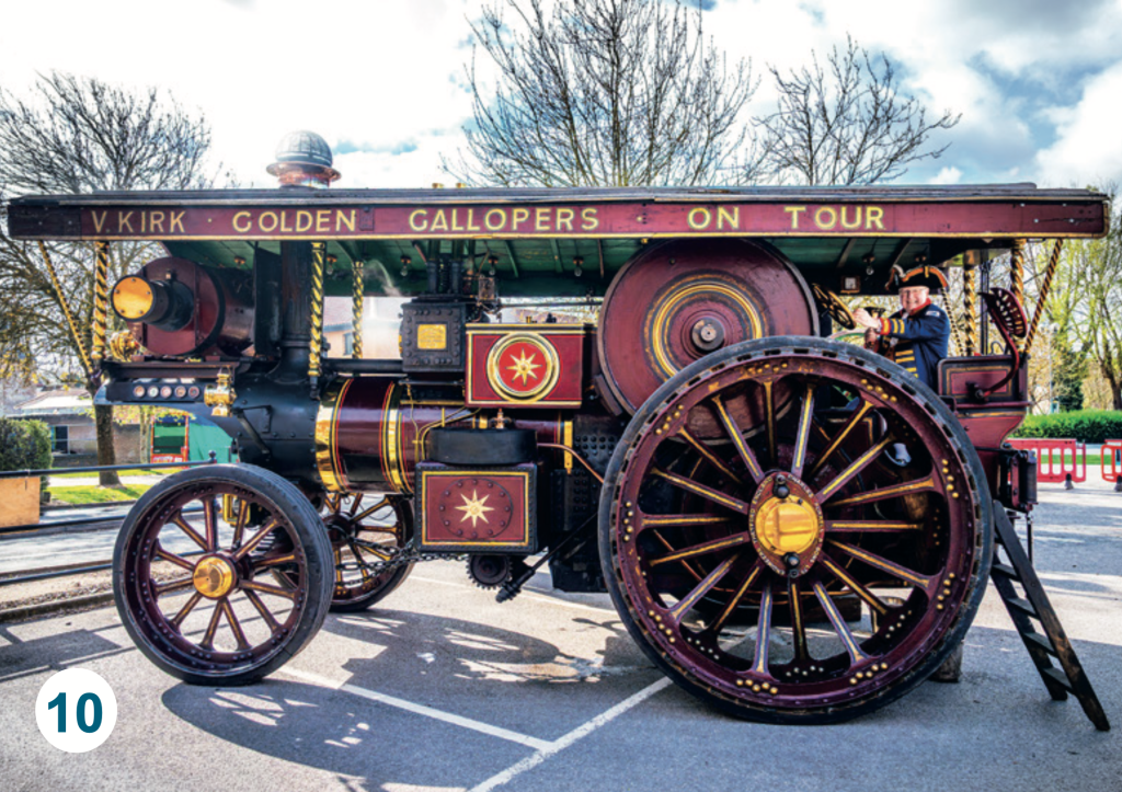 A historic steam traction engine named "Golden Gallopers – On Tour", parked outdoors with ornate red, black and gold detailing and its driver seated at the controls.