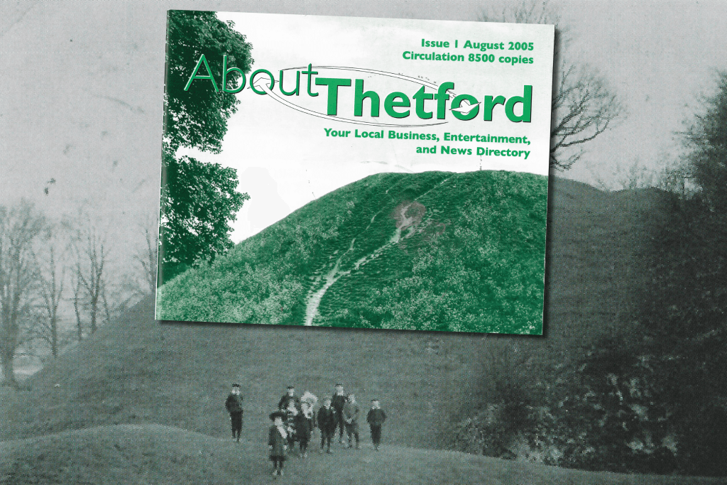 A vintage photograph of Thetford's Castle Hill in black and white forms the background, with a group of children in Edwardian-style clothing standing on the grassy mound. Overlaid on the hill is a colour image of the first ever cover of About Thetford magazine (Issue 1, August 2005), featuring a green-tinted photo of the same hill and the tagline: “Your Local Business, Entertainment, and News Directory.”