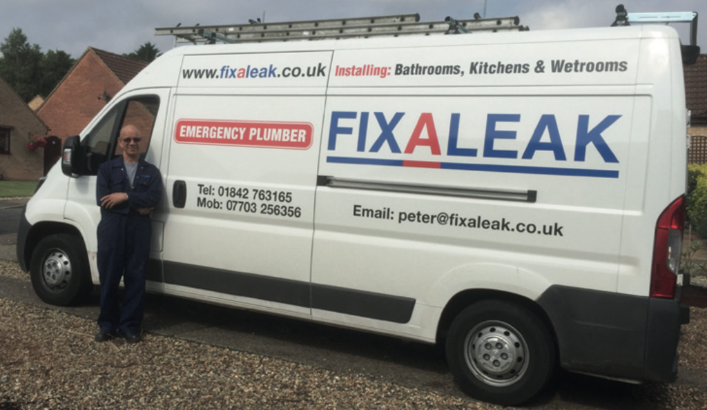 Fixaleak plumber standing next to a white work van. Van signage shows company website www.fixaleak.co.uk , email peter@fixaleak.co.uk , telephone 01842 763165, mobile 07703 256356. Red ‘Emergency Plumber’ box is visible along with the Fixaleak logo. The van also advertises installation of bathrooms, kitchens and wetrooms. The man is wearing blue overalls, sunglasses, and is smiling with arms crossed.
