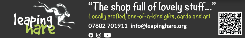 A dark grey banner with the Leaping Hare logo showing a stylised white hare leaping. The text reads: “The shop full of lovely stuff…” Locally crafted, one-of-a-kind gifts, cards and art. Contact details are shown: 07802 701911 and info@leapinghare.org
. Icons for Facebook, Instagram and YouTube appear, along with a QR code on the right-hand side.