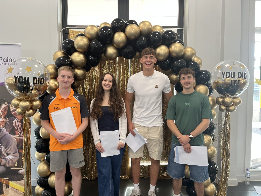 Four students pose with results envelopes under the same black and gold balloon arch, with “You Did It!” balloons on either side.