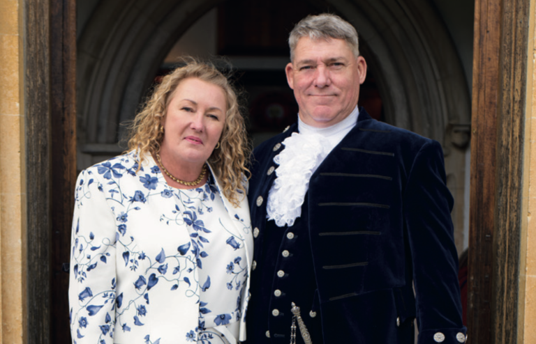 Jo Pearson stands with his wife Mandy at his High Sheriff installation ceremony, both dressed formally, with Jo wearing traditional ceremonial attire including a lace jabot, outside a historic building. Image credit: Georgie Pearson.