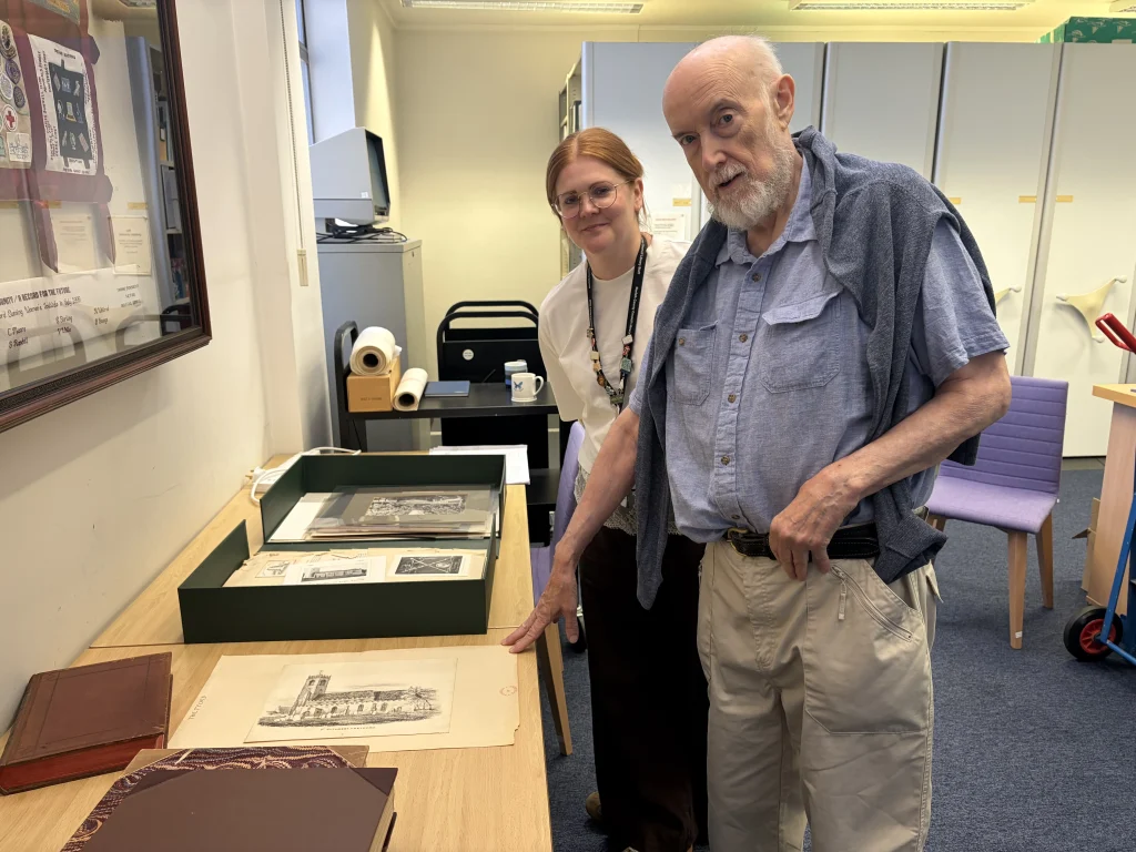 Two people examine historic Thetford documents and illustrations laid out on a table in a local archive or library.