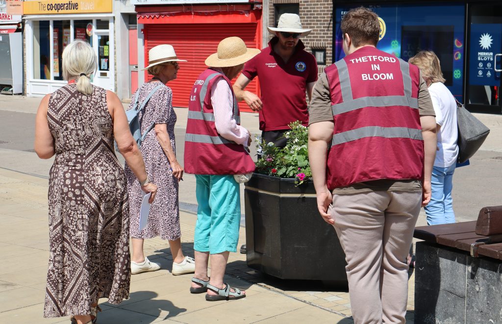 Anglia in Bloom judges meet Thetford Town Council officers and volunteers beside a flower-filled planter in the town centre.