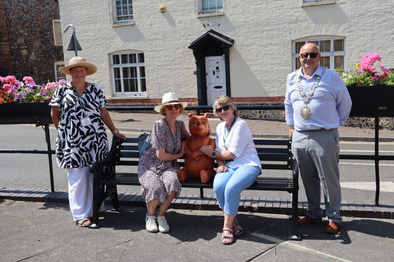 Anglia in Bloom judges pose with Thetford Mayor Cllr Vic Peters beside the newly installed bear bench, surrounded by colourful floral displays.